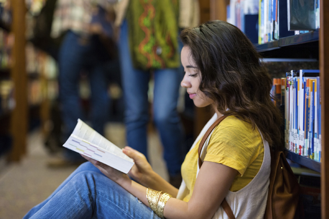 Hispanic college student sitting in library reading books - Stock